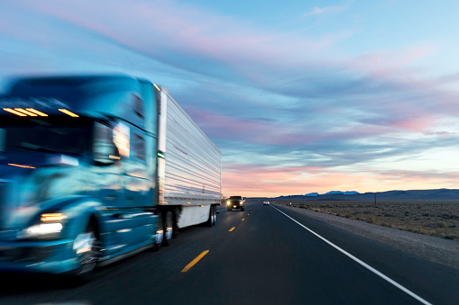 Stock photo from a driver of a vehicles point of view at sunset on a highway with passing cars and trucks.