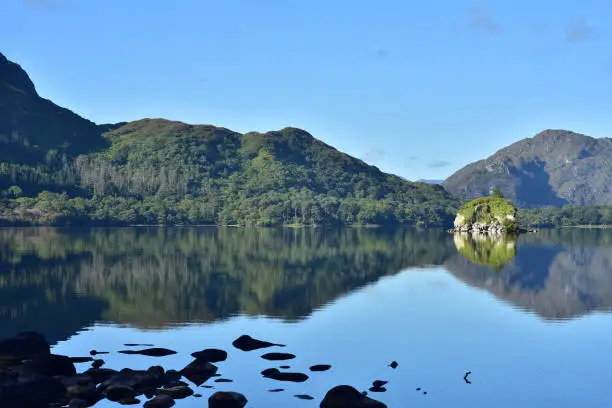 Surrounding country reflections on completely calm surface of Muckross Lake in Ireland in morning light.
