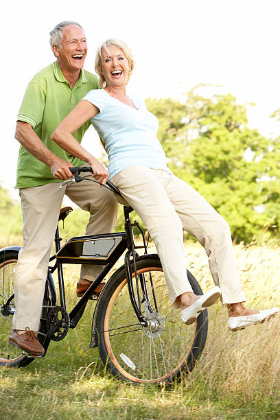 coppia matura equitazione bicicletta nella campagna - mature adult bicycle senior adult heterosexual couple foto e immagini stock