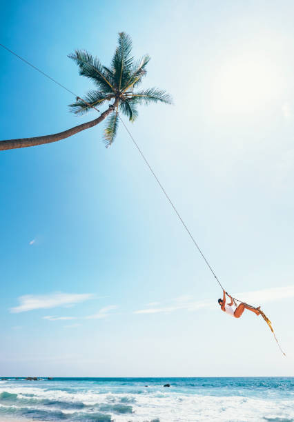 istock Woman dangles on tropical palm tree swing over ocean waves 950588124