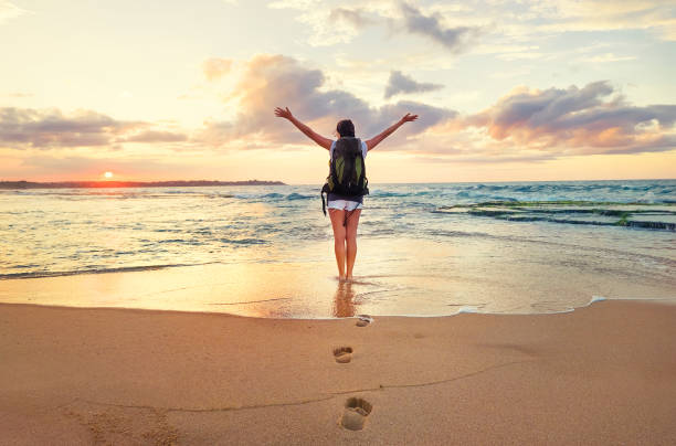 istock Woman backpacker stay on ocean surf line at sunset time 950588176