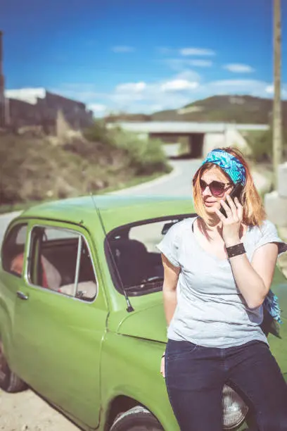 A ginger girl talking on her phone next to her restorated green supermini car