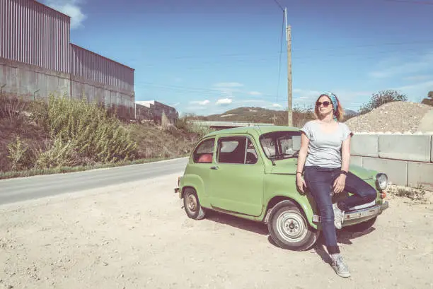 A ginger girl sitting on the side of her restorated green supermini automobile