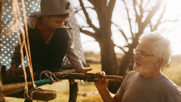 Photo of a grandfather and his grandson, building a tree house on a beautiful sunny day they are spending outdoors in nature // wide photo dimensions