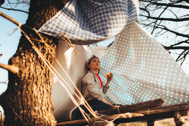 Photo of a young boy, proud tree house owner, sitting up on his property and having a healthy snack
