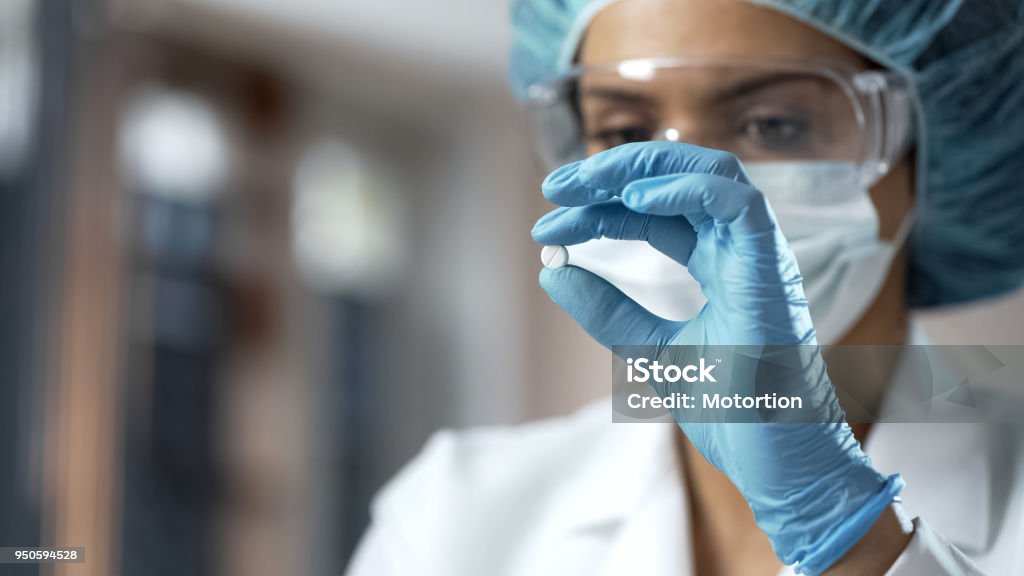 Female chemist looking at white pill, new medication testing in laboratory Medicine Stock Photo