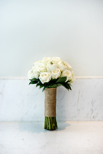 Bride's bouquet on the white wall made with flowers white cream roses tie the handle with rope