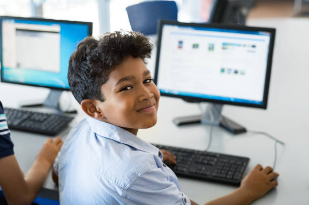 School boy using computer Young happy schoolboy using computer to search internet. Arab child learning to use computer at elementary school. Portrait of smiling middle eastern kid looking at camera while surfing the net in school library. schoolboy stock pictures, royalty-free photos & images
