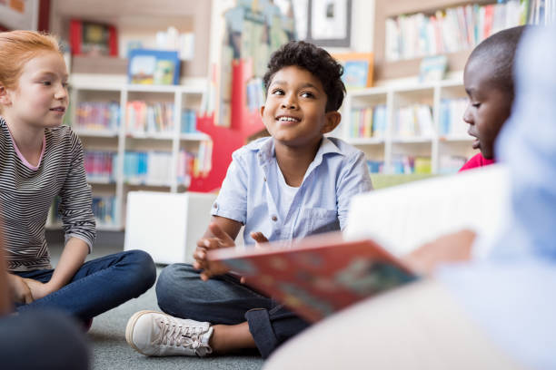 Children listening stories Multiethnic group of kids sitting on floor in circle around the teacher and listening a story. Discussion group of multiethnic children in library talking to woman. Portrait of smiling hispanic boy in elementary school. stock libraries stock pictures, royalty-free photos & images