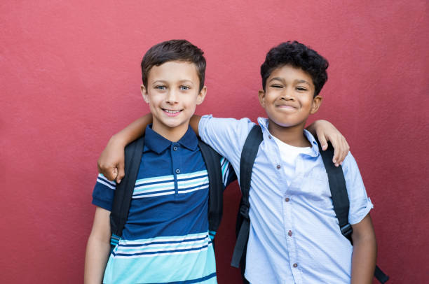 Smiling children friends embracing Best children friends standing with hand on shoulder against red background. Happy smiling classmates standing together on red wall after school. Portrait of multiethnic schoolboys enjoying friendship. pre adolescent child stock pictures, royalty-free photos & images