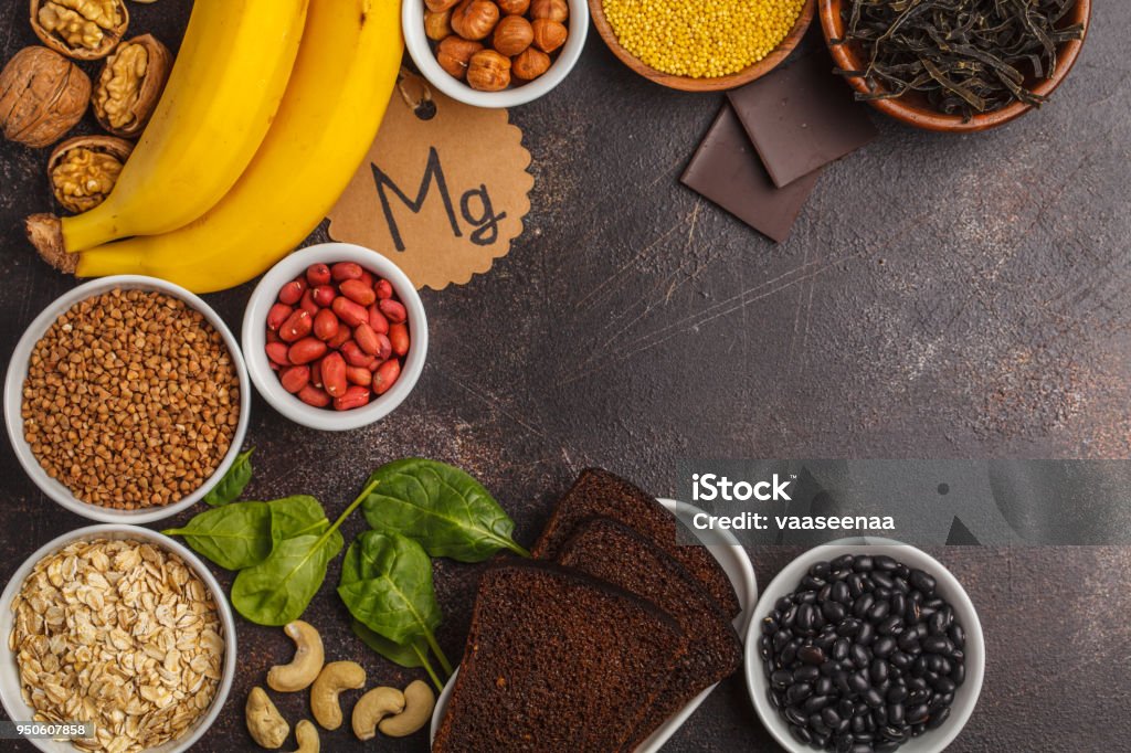 Healthy food nutrition dieting concept. Assortment of high magnesium sources. Banana chocolate spinach, buckwheat, nuts, beans, oat. Dark background, copy space Healthy food nutrition dieting concept. Assortment of high magnesium sources. Banana chocolate spinach, buckwheat, nuts, beans, oat. Magnesium Stock Photo