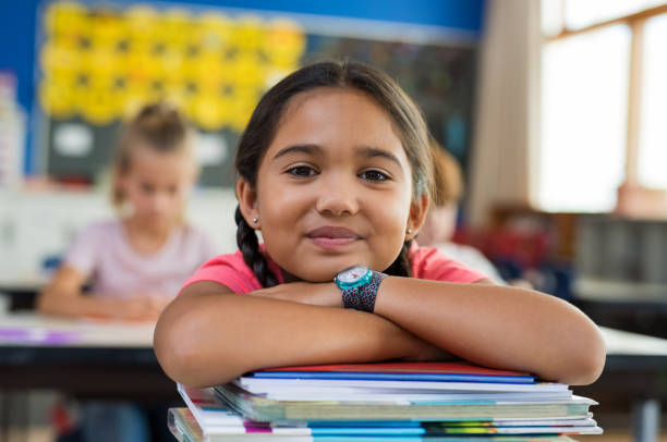 Hispanic girl with chin on books Portrait of cute little schoolgirl leaning on stacked books in classroom. Happy young latin girl in casual keeping chin on notebooks. Closeup face of smiling girl at elementary school. school child stock pictures, royalty-free photos & images