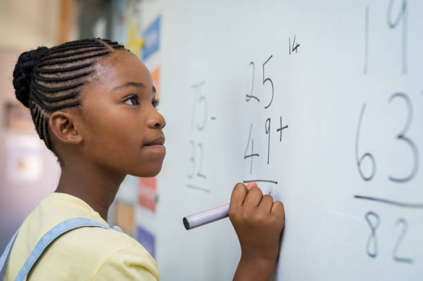 Girl solving mathematical addition Portrait of african girl writing solution of sums on white board at school. Black schoolgirl solving addition sum on white board with marker pen. School child thinking while doing mathematics problem. elementary school stock pictures, royalty-free photos & images