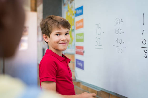 Boy doing math sum Clever boy doing sums on white board and looking at camera. Smiling schoolboy solving addition and subtraction sum in mathematics lesson. Proud young boy standing with math operation solved. kids using smart board stock pictures, royalty-free photos & images