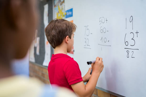 Boy solving math problem Rear view of young boy solving addition and subtraction on white board at school. Schoolboy thinking while solving math's sum. Smart child writing the solution of the mathematical operation in classroom. kids using smart board stock pictures, royalty-free photos & images