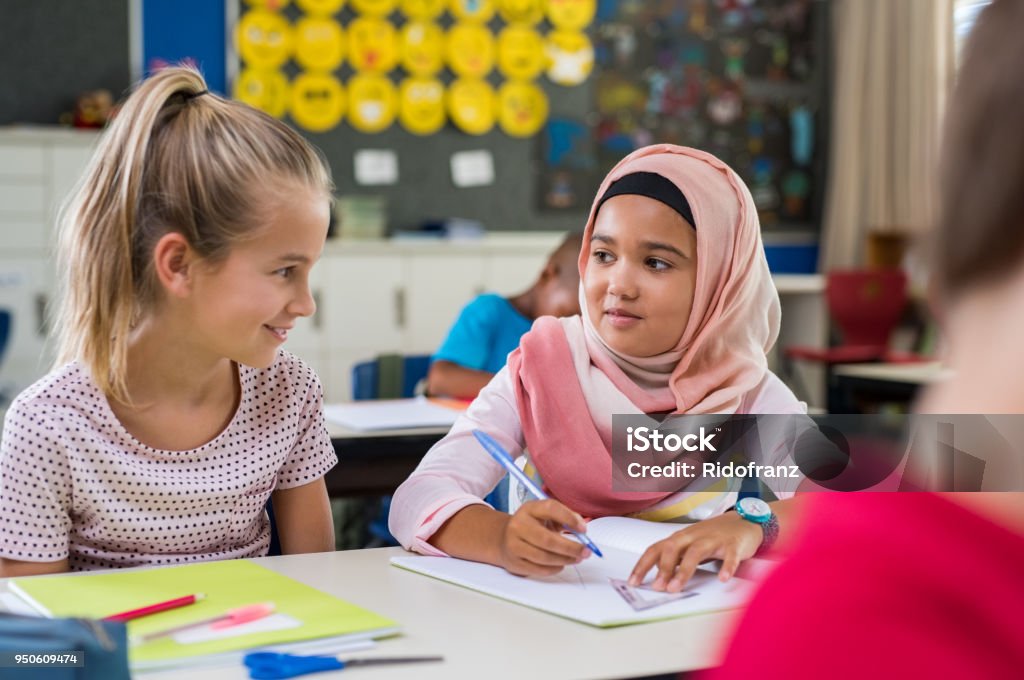 Muslim girl with her classmate Young arab girl with hijab doing exercise with her bestfriend at international school. Asian muslim school girl sitting near her classmate during lesson. Multiethnic elementary students in classroom. Child Stock Photo