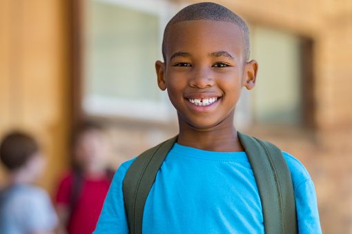 Smiling african american school boy with backpack looking at camera. Cheerful black kid wearing green backpack with a big smile. Elementary and primary school education.