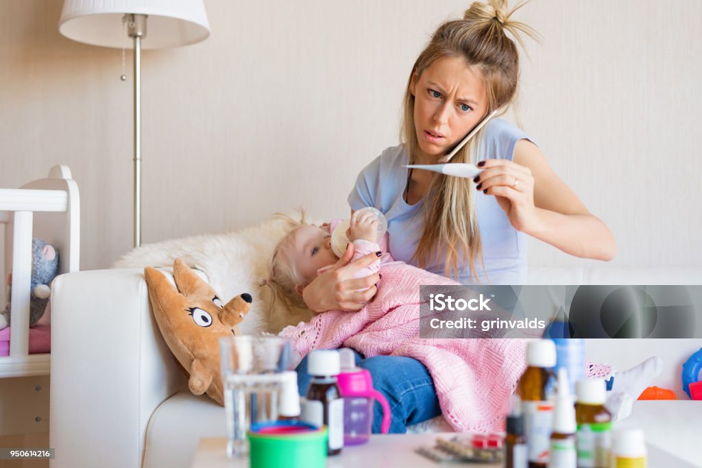 Woman with sick baby calling doctor Woman with sick baby calling doctor. Worried mom looking at thermometer showing high temperature of her little child and calling doctor for advice. Child Stock Photo