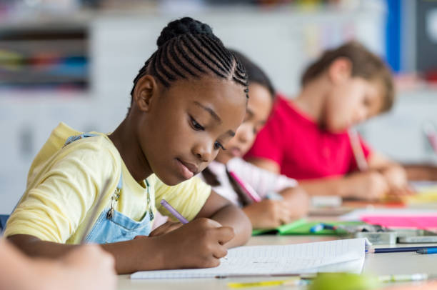 School girl writing in class Cute pupil writing at desk in classroom at the elementary school. Student girl doing test in primary school. Children writing notes in classroom. African schoolgirl writing on notebook during the lesson. elementary school stock pictures, royalty-free photos & images