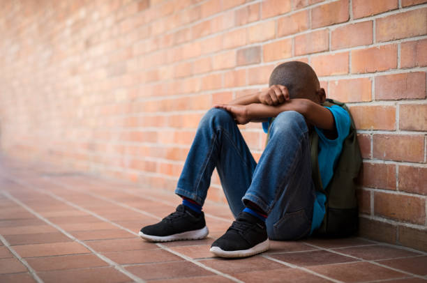 Young sad boy at school Young boy sitting alone with sad feeling at school. Depressed african child abandoned in a corridor and leaning against brick wall. Bullying, discrimination and racism concept at school with copy space. african american kids stock pictures, royalty-free photos & images