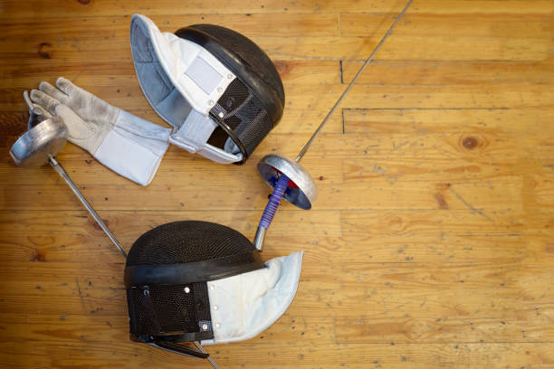 Fencing mask, gloves, swords and epees lie on the floor in the fencing gym
