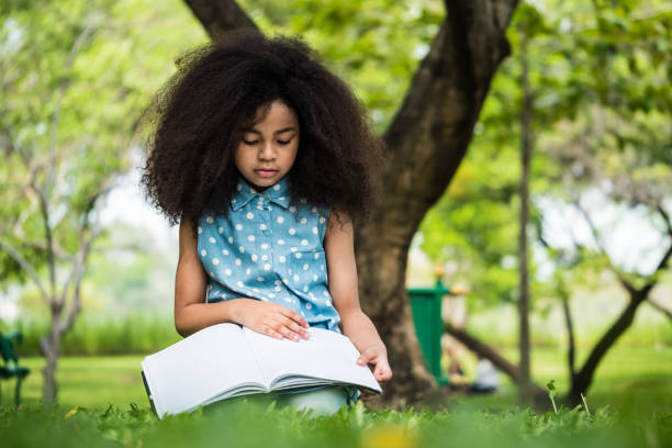 istock Beautiful girl reading a book while sitting on green grass in a park 950616156