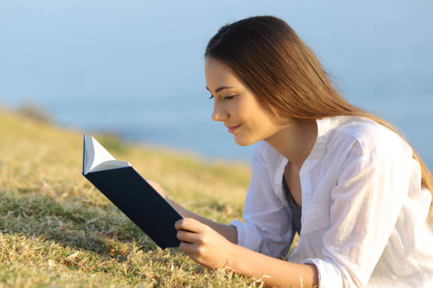 istock Relaxed woman reading a paper book lying on the grass 950628012