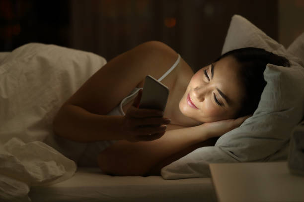 jeune fille à l’aide d’un téléphone intelligent sur le lit dans la nuit - bed child smiling people photos et images de collection
