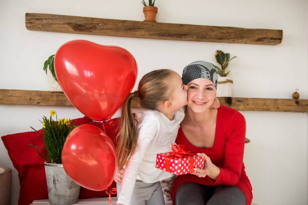 giovane madre, paziente oncologa e sua figlia carina, che festeggiano il ritorno a casa dall'ospedale. bentorna a casa o festa di compleanno con palloncini e regali. - cancer chemotherapy drug baby family foto e immagini stock