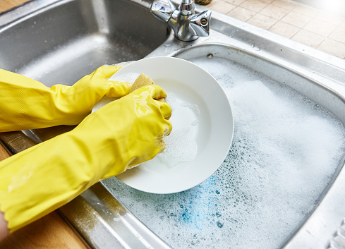 Wearing protective gloves, a woman's hands wash the dishes.