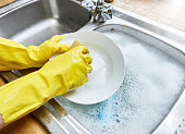 Gloved hands wash the dishes in kitchen sink.
