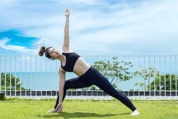 Happy Asian woman wearing black sport wear practice yoga Triangle pose with beautiful sea view,Feeling relax and comfortable,Healthy Concept