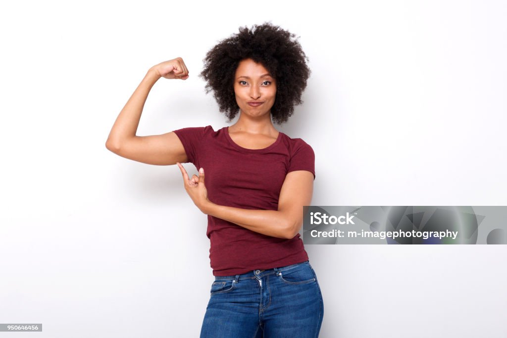 fit young african woman pointing at arm muscles on white background Portrait of fit young african woman pointing at arm muscles on white background Girl Power Stock Photo