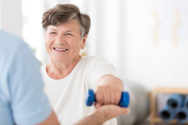 Senior woman exercising with weights Happy senior woman exercising arms with small weights with help from a physiotherapist and copy space osteoporosis stock pictures, royalty-free photos & images
