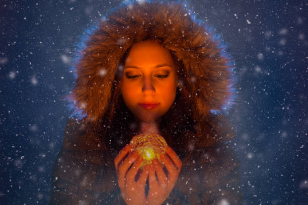 Young woman with magic glowing lantern in hands at night during a snowstorm