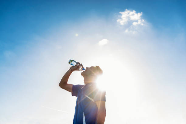 Guy after exercise, drinking water on the football field. Portrait of handsome man in sportswear. Photo of soccer player drinking water,  refreshing during break on soccer field during bright sunny day.