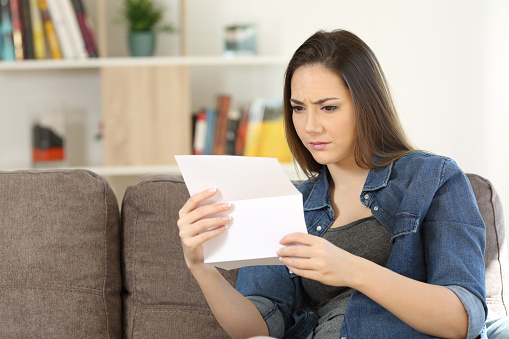 Worried woman reading a letter sitting on a couch in the living room at home