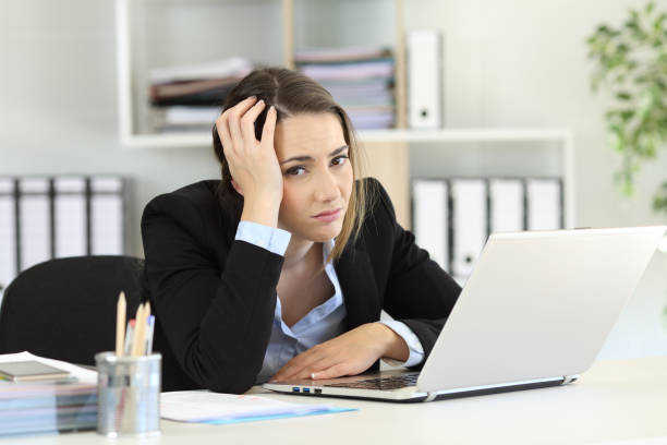 Worried office worker looking at camera Worried office worker looking at camera sitting in a desk at workplace melancholy computer support specialist stock pictures, royalty-free photos & images