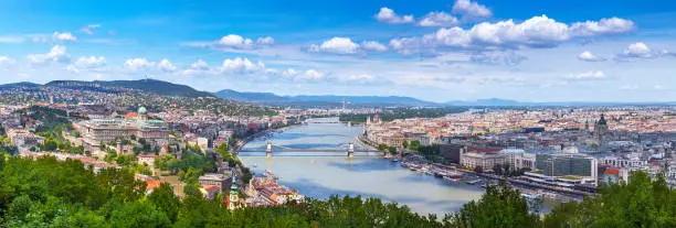 Photo of Panoramic cityscape view of hungarian capital city of Budapest from the Gellert Hill. The bridges connecting Buda and Pest across the river Danube. Summertime sunshine day, blue sky and green of trees