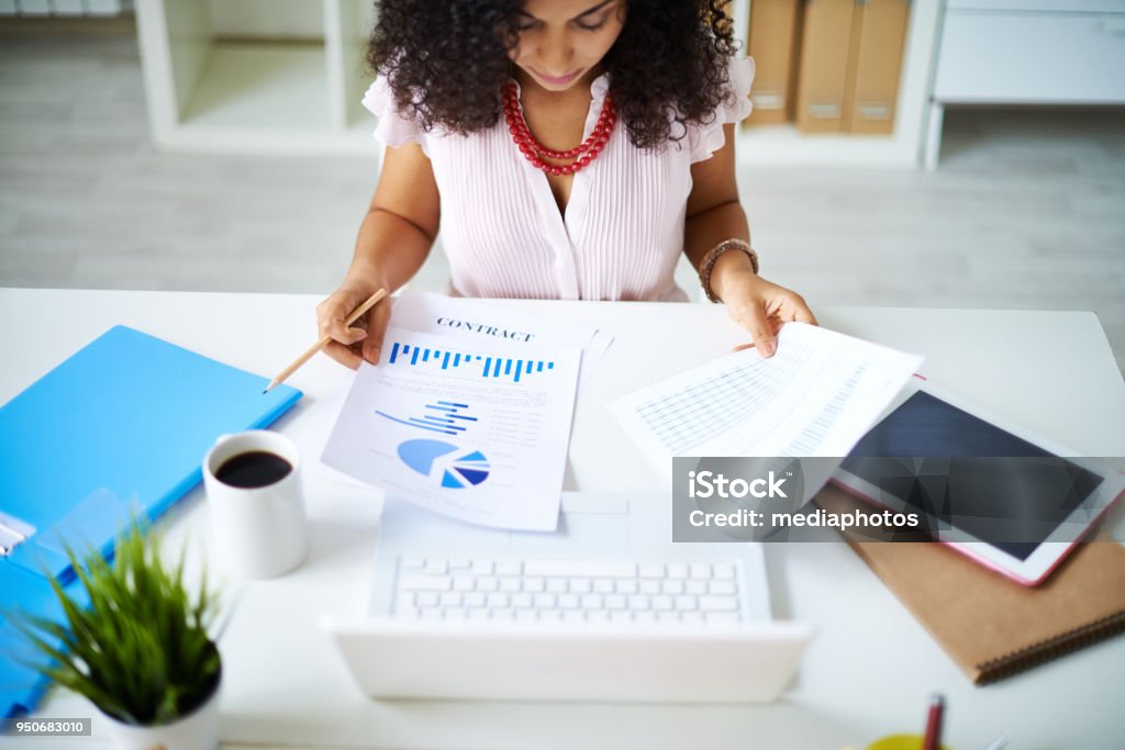 Preparing project report Businesswoman examining documents sitting at office table Financial Report Stock Photo