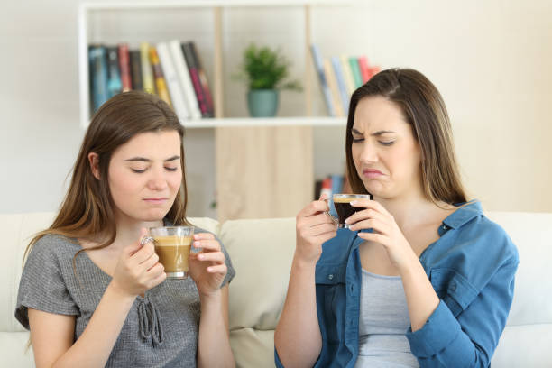 Two friends drinking coffee with bad flavour Two friends drinking coffee with bad flavour sititng on a couch in the living room at home bad coffee stock pictures, royalty-free photos & images
