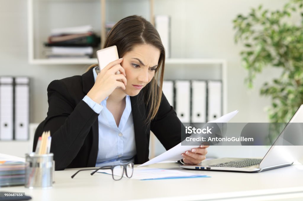 Angry executive calling on phone at office Angry executive calling on phone reading a paper document at office Office Stock Photo