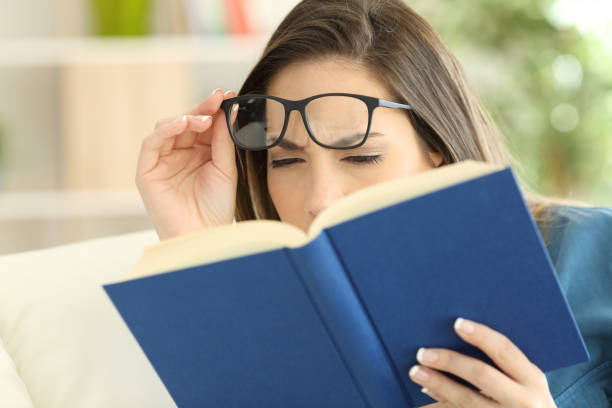 Woman suffering eyestrain reading a book Woman suffering eyestrain trying to read a book at home myopia photos stock pictures, royalty-free photos & images