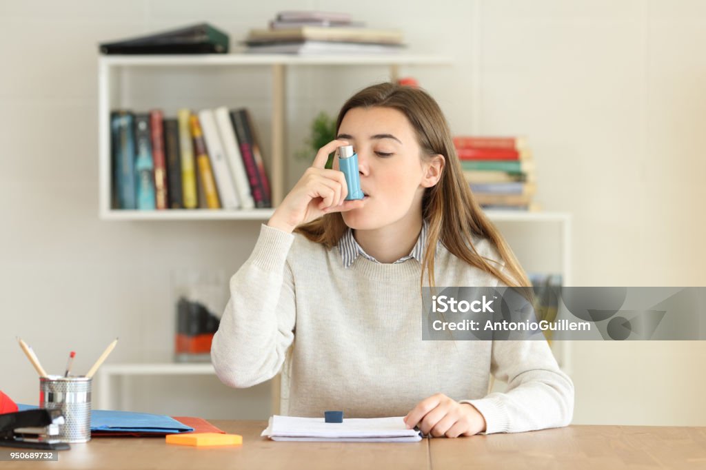 Student using an asthma inhaler at home Student having an asthma attack using an asthma inhaler at home Asthmatic Stock Photo