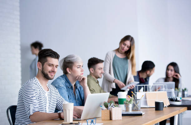 People in open space office Woman by a desk looking outside among a group of young people collaborating in an open space start-up office cd writer photos stock pictures, royalty-free photos & images