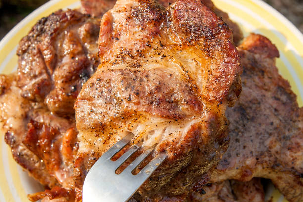 Pork steak on fork cooked on an open flame grill