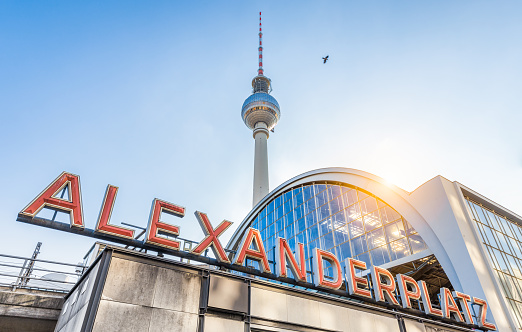 Wide-angle view of Alexanderplatz neon sign with famous TV tower and train station in golden evening light at sunset in summer, central Berlin Mitte district, Germany