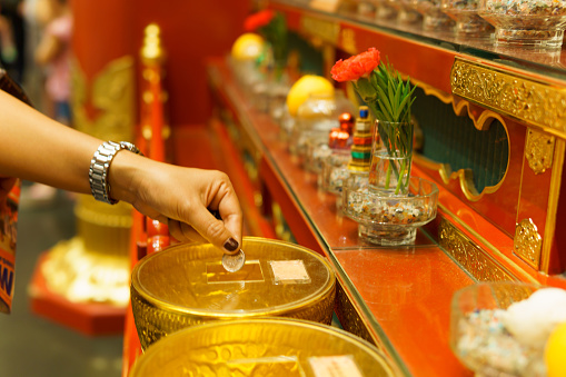 asian female hand drop coin in to the golden bowl to pay a merit in the Buddha Tooth Relic Temple and Museum