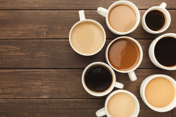 Different types of coffee in cups on wooden table, top view