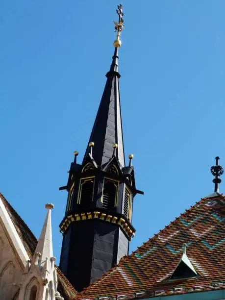 Black church tower and colorful ceramic clay tile roof below and blue sky above